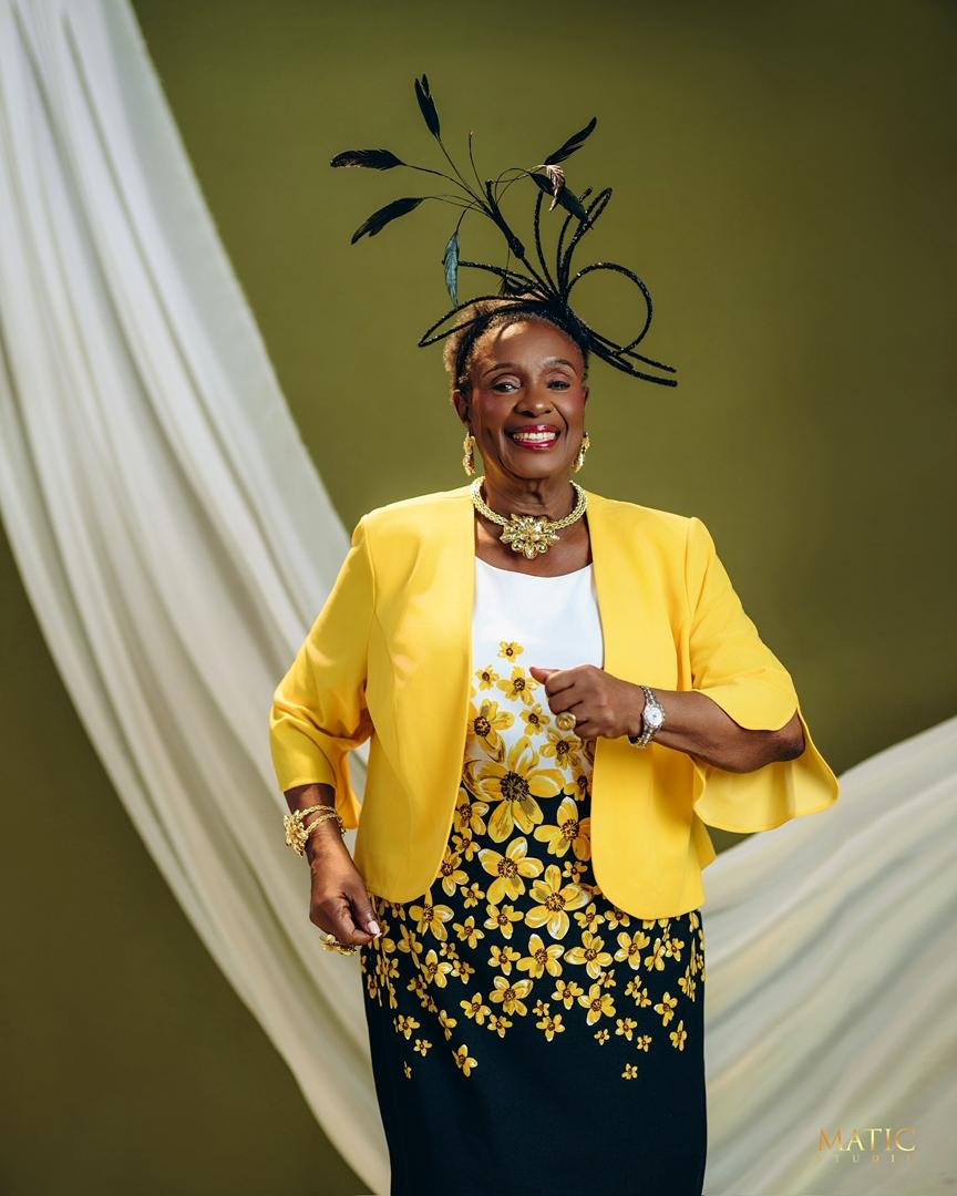 Chief Mrs. Josephine Chinyelu Nwosu standing in a yellow jacket and floral dress.