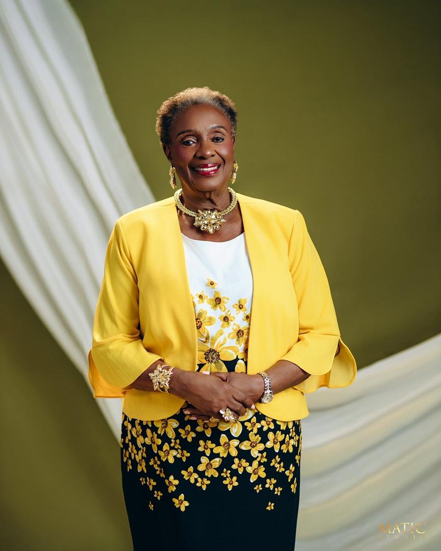 Chief Mrs. Josephine Chinyelu Nwosu smiling in a yellow jacket and floral dress.